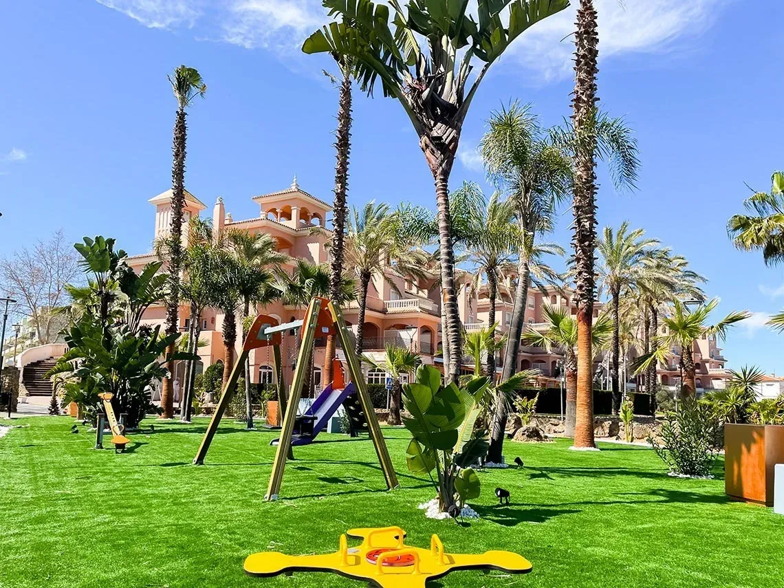 Zona infantil con columpio y tobogán, palmeras y edificio ON Family Playa Doñana | ON Hotels Group.