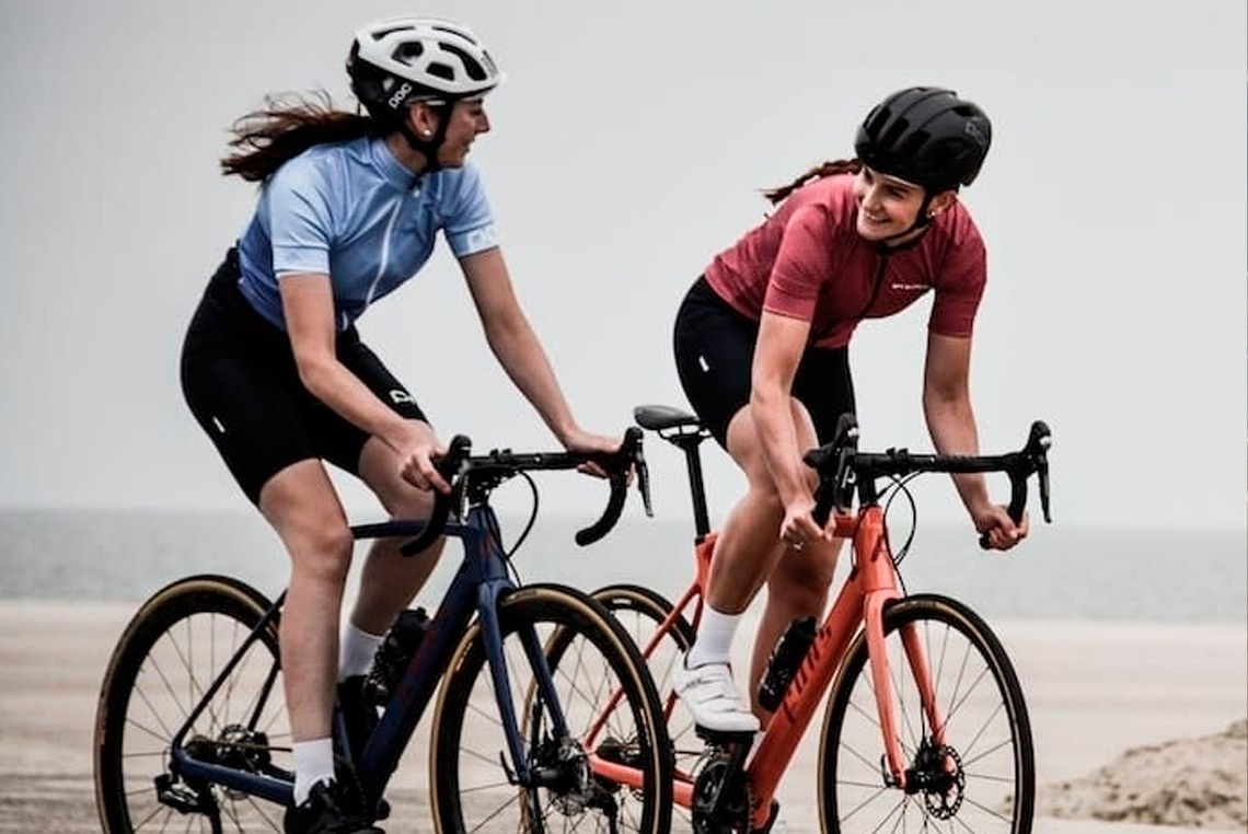 two women wearing helmets are riding bicycles on the beach