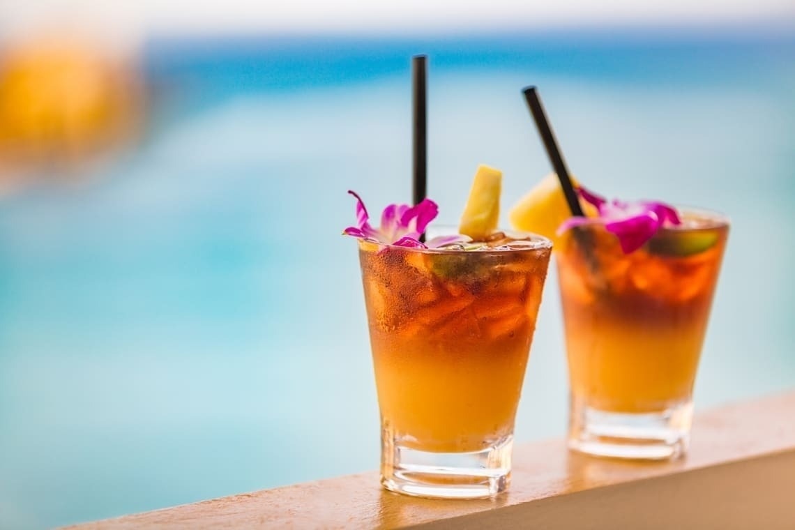 deux cocktails avec des pailles et des fleurs sont assis à côté d' une piscine