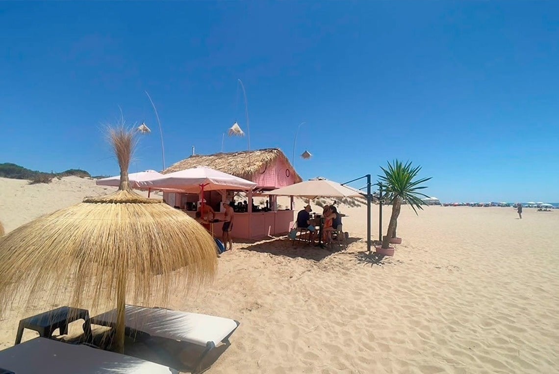 uma praia com um bar rosa e guarda-chuvas