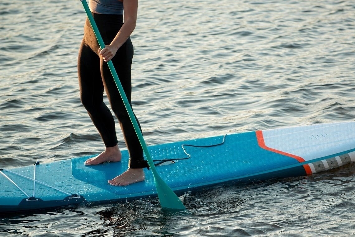 eine Frau paddelt auf einem blauen und weißen Surfbrett