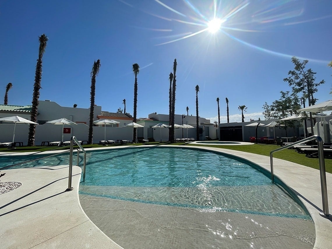una piscina rodeada de palmeras y sombrillas en un día soleado