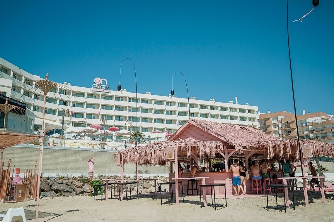 un bar en la playa con un hotel en el fondo