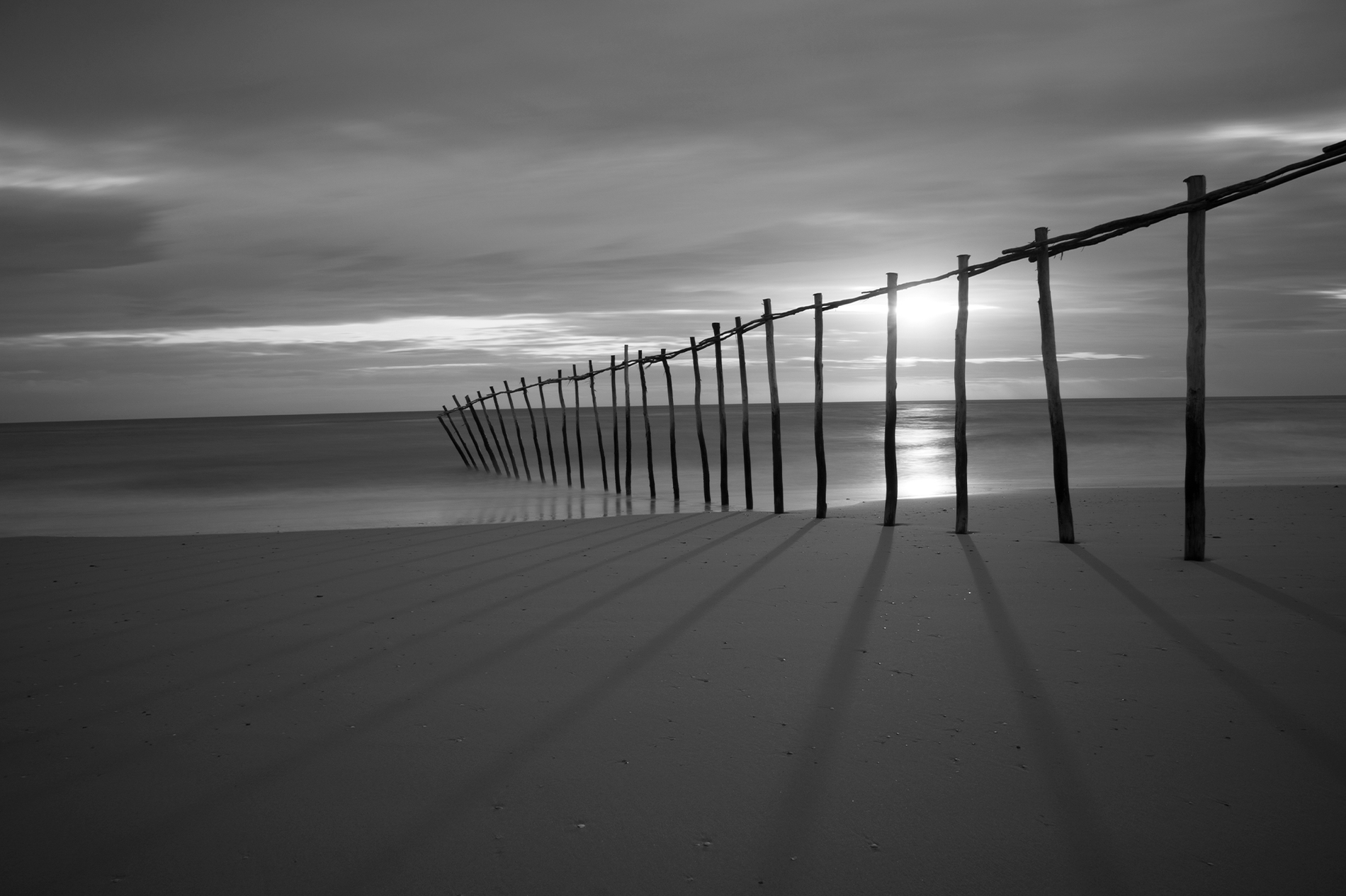 ein Schwarz-Weiß-Foto eines Holzzauns am Strand=s1900