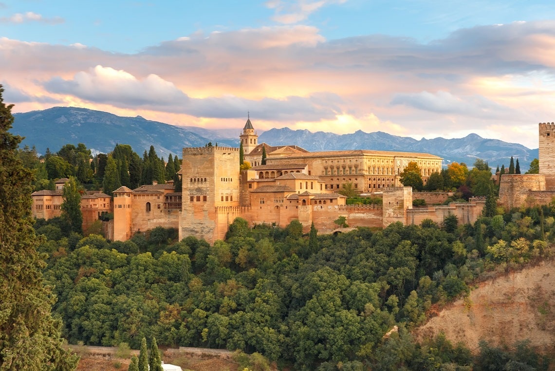 um grande castelo está situado no topo de uma colina com montanhas ao fundo