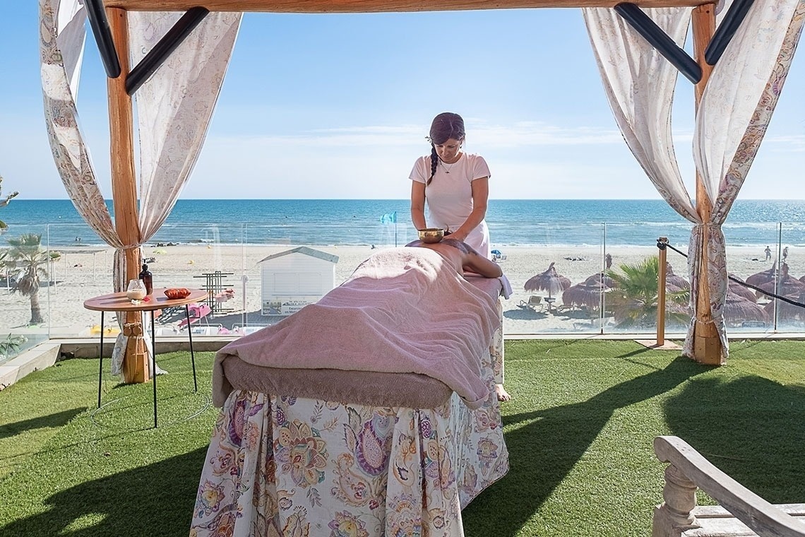 una mujer da un masaje a una mujer en una cama con vista al océano