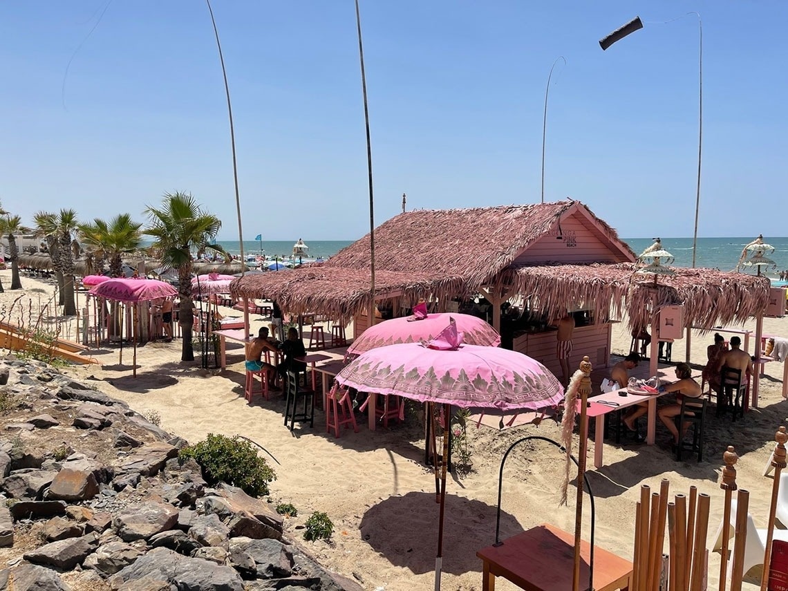 a pink thatched hut on a beach with tables and chairs