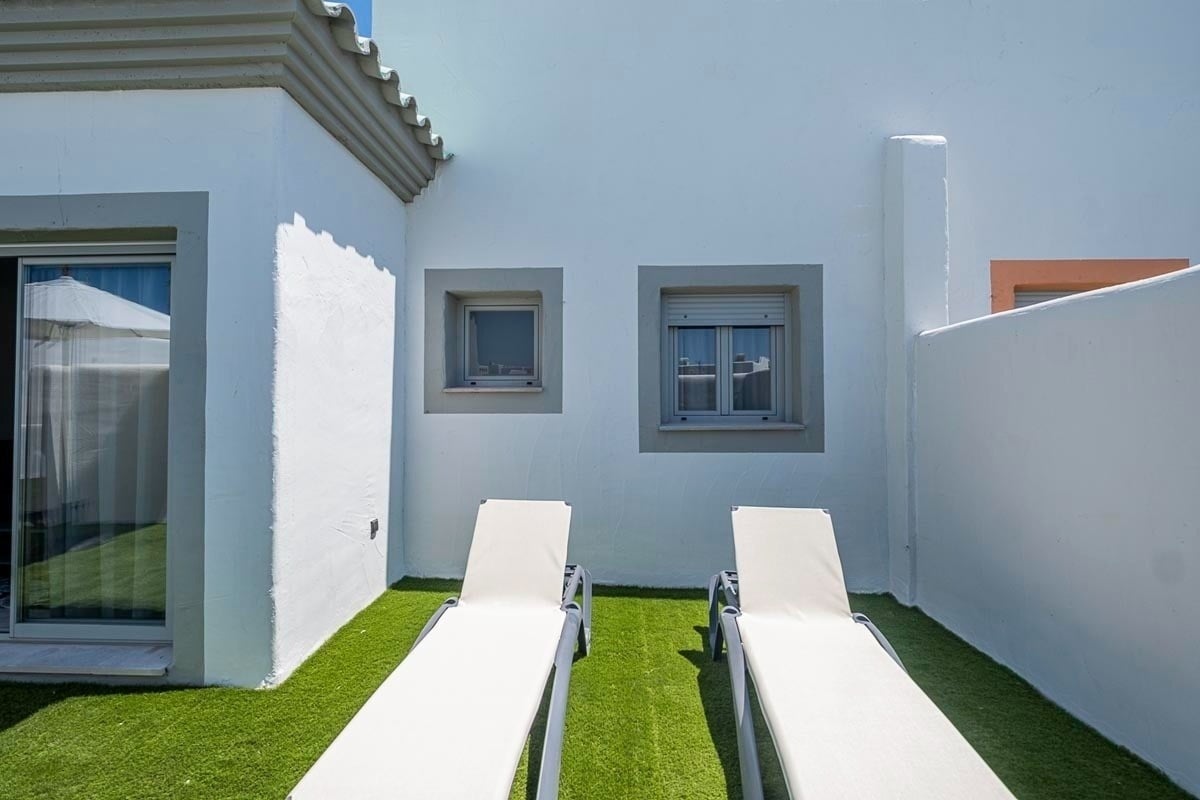 two white lounge chairs sit on a lush green lawn in front of a white building
