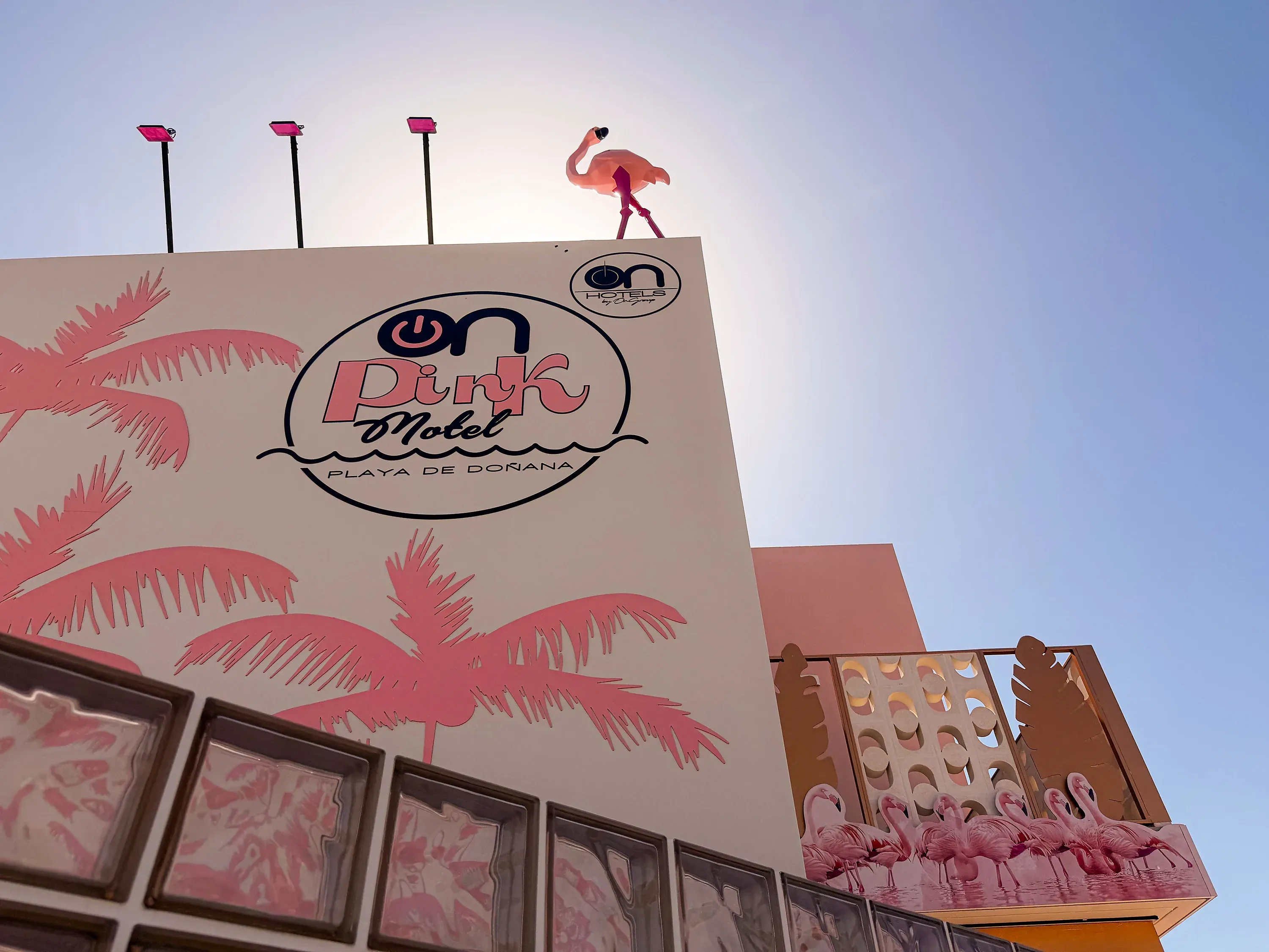ON Pink Motel | Matalascañas: Fachada del hotel ON Pink Motel Playa de Doñana, con flamencos y palmeras rosas.