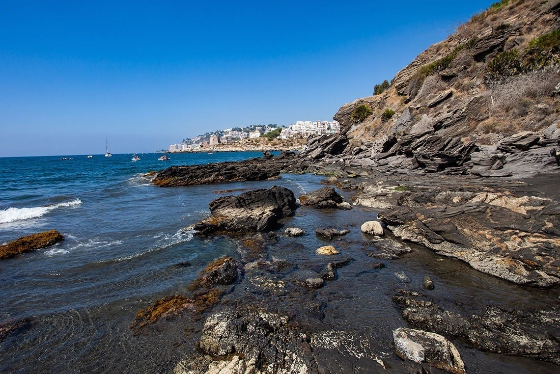 una playa con muchas rocas y un pueblo en el fondo