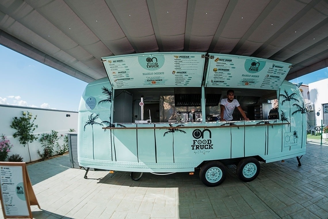 un camion de nourriture est assis à côté d' une piscine entourée d' tables et d' parasols