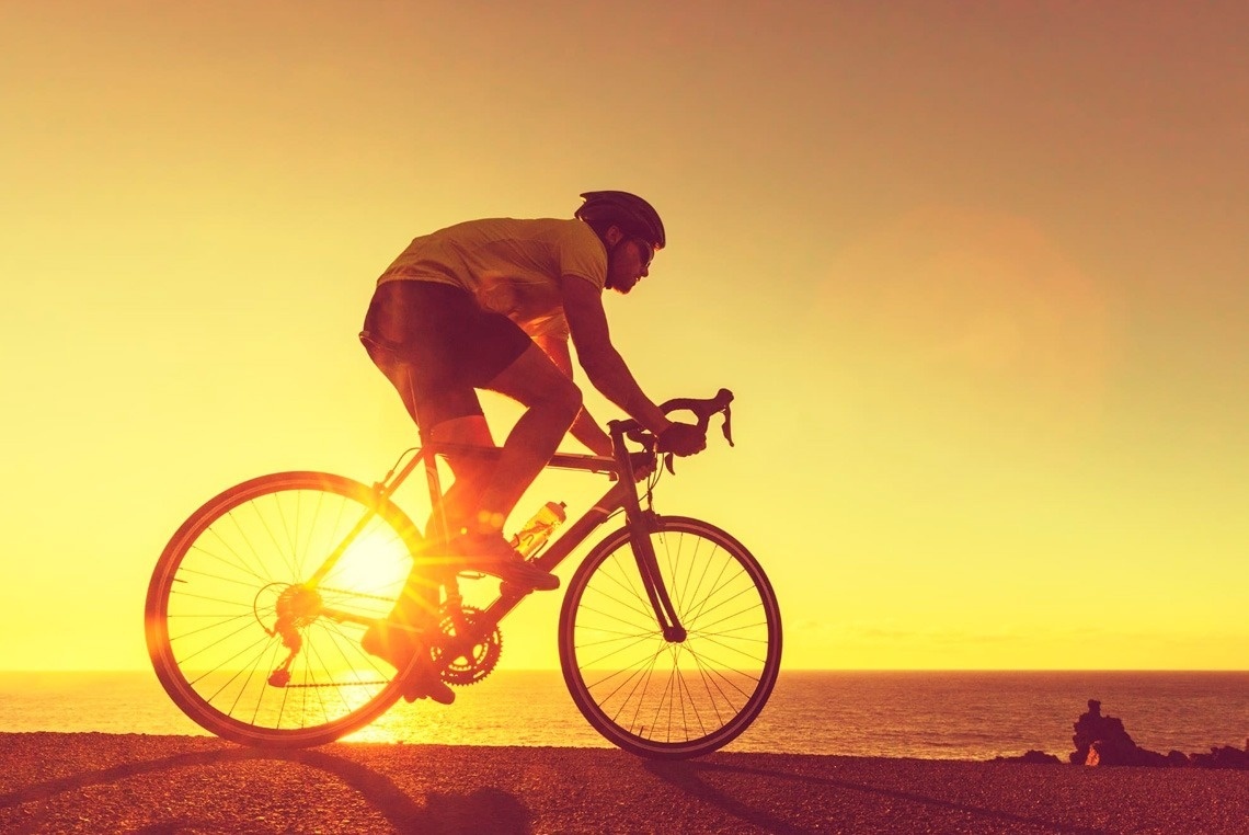 a man in a yellow shirt is riding a bike at sunset
