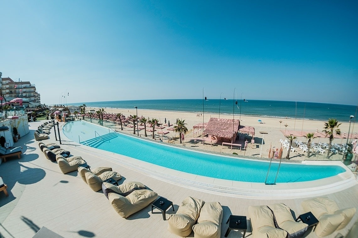 una gran piscina está rodeada de sillas y mesas en una playa