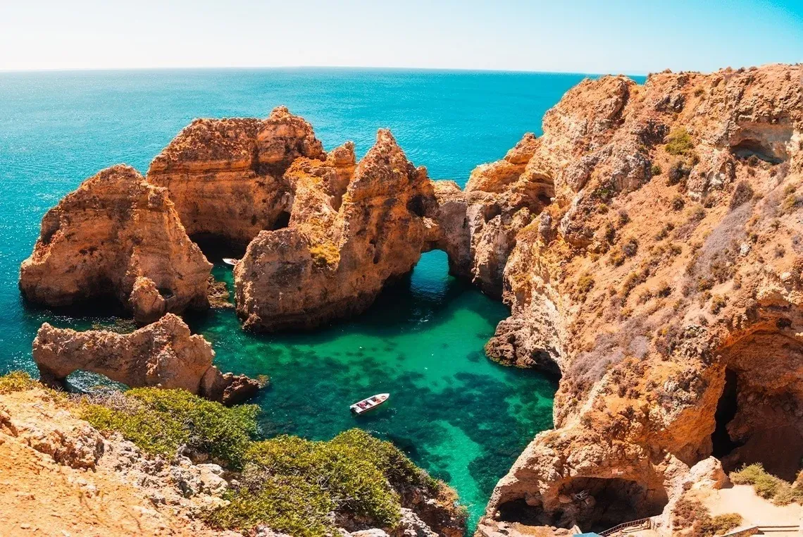 Acantilados dorados, agua turquesa y bote en Ponta da Piedade. On Hotels: ON Corporativa.
