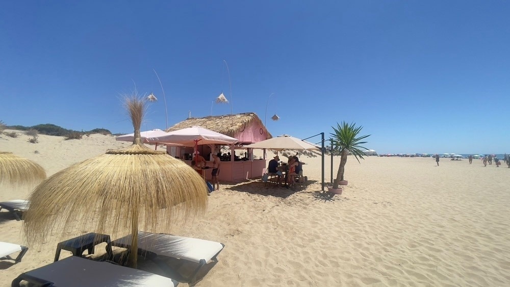 a pink hut with straw umbrellas on the beach
