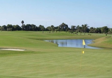 un campo de golf con una bandera amarilla y un estanque en el medio .