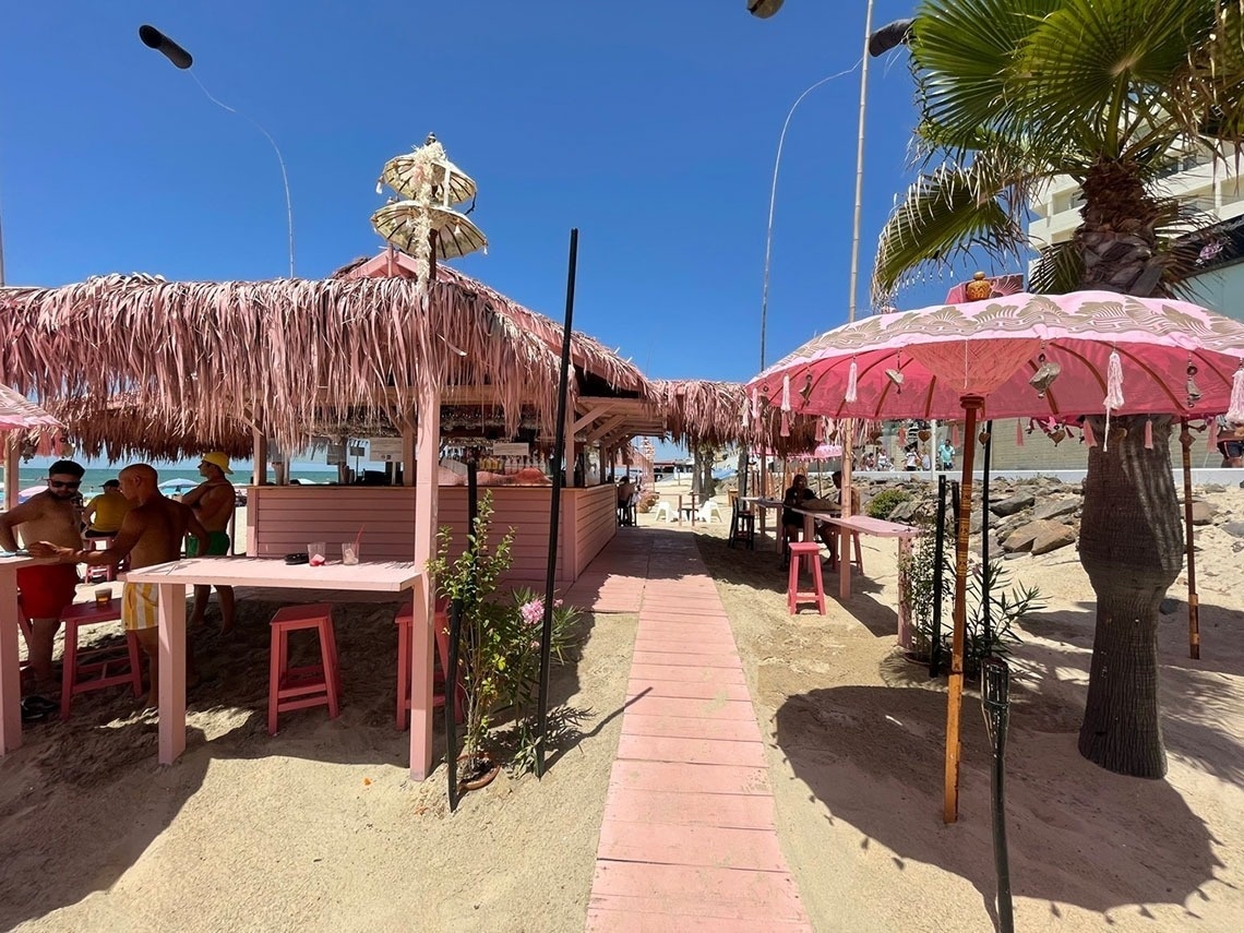 a beach bar with pink umbrellas and straw roofs