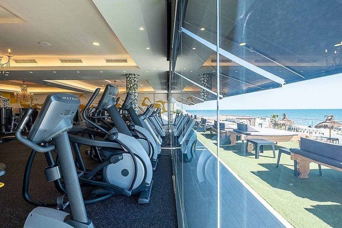 una fila de máquinas de ejercicio en un gimnasio junto a una ventana con vista al océano