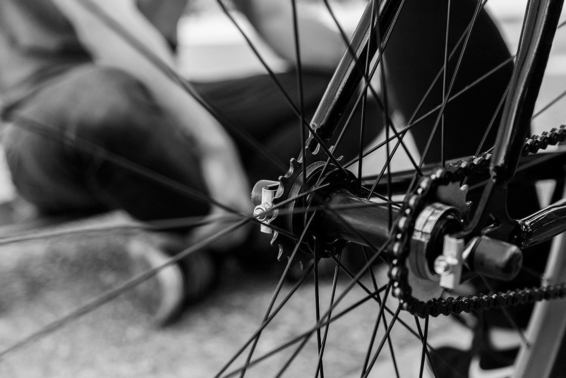 uma foto em preto e branco de uma pessoa reparando uma bicicleta