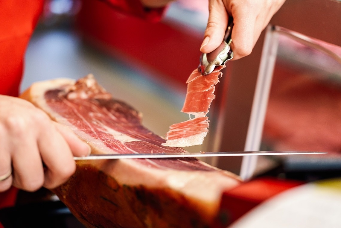 una persona corta un trozo de jamón con un cuchillo