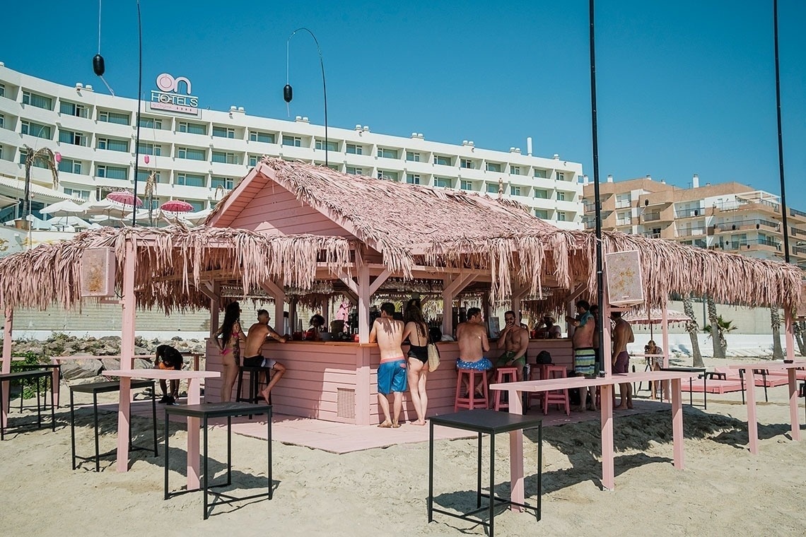 un bar rosa en la playa con un hotel en el fondo