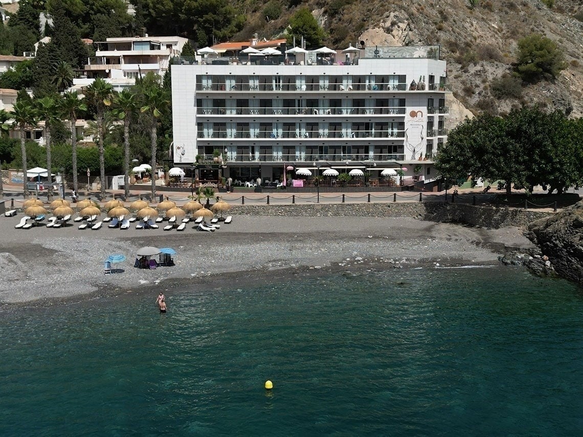 una playa con sillas y sombrillas y un hotel en el fondo