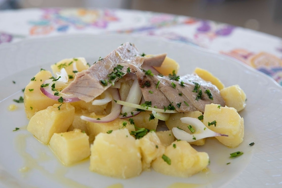 un plato blanco lleno de patatas y atún sobre una mesa