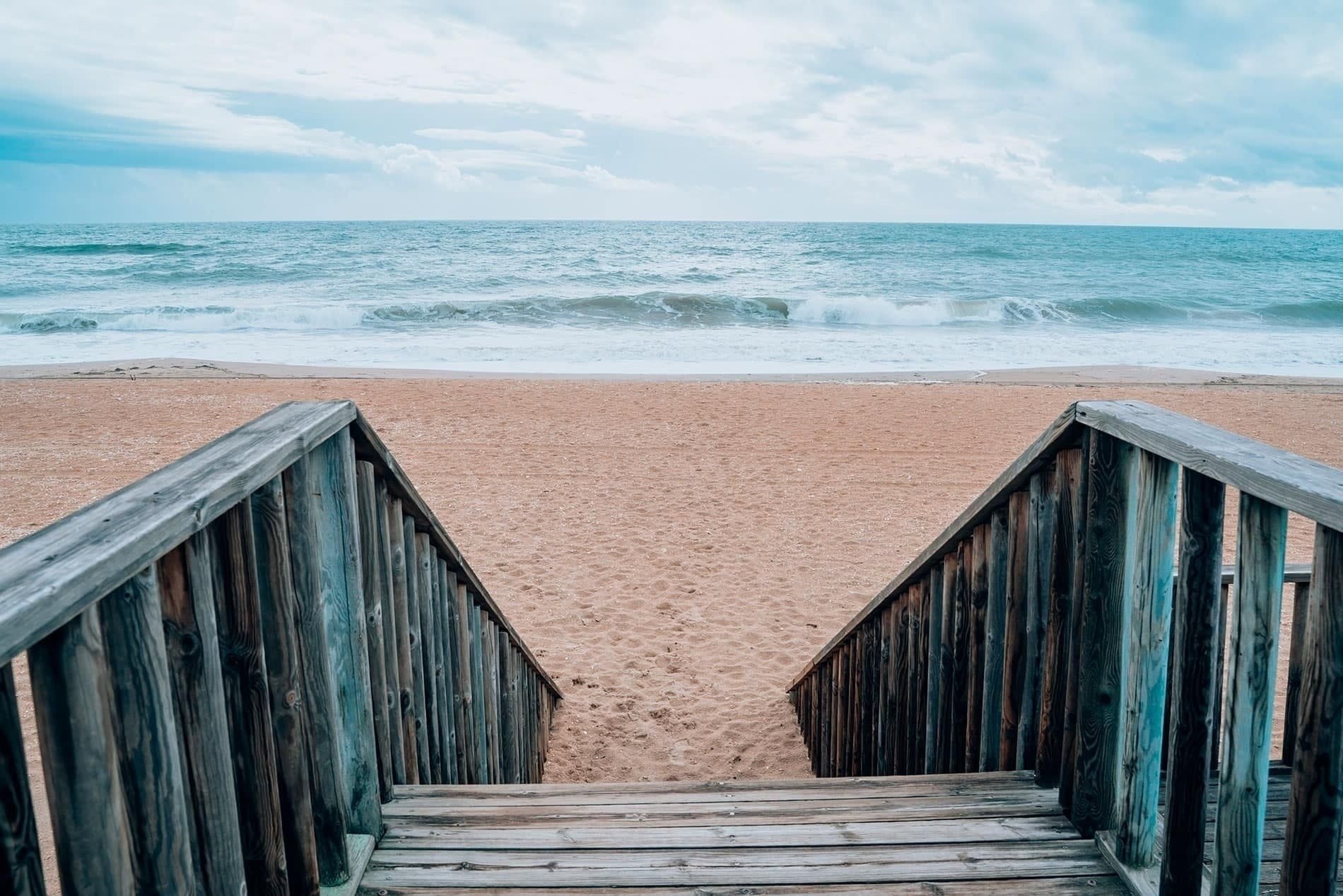 una escalera de madera conduce a una playa de arena al océano