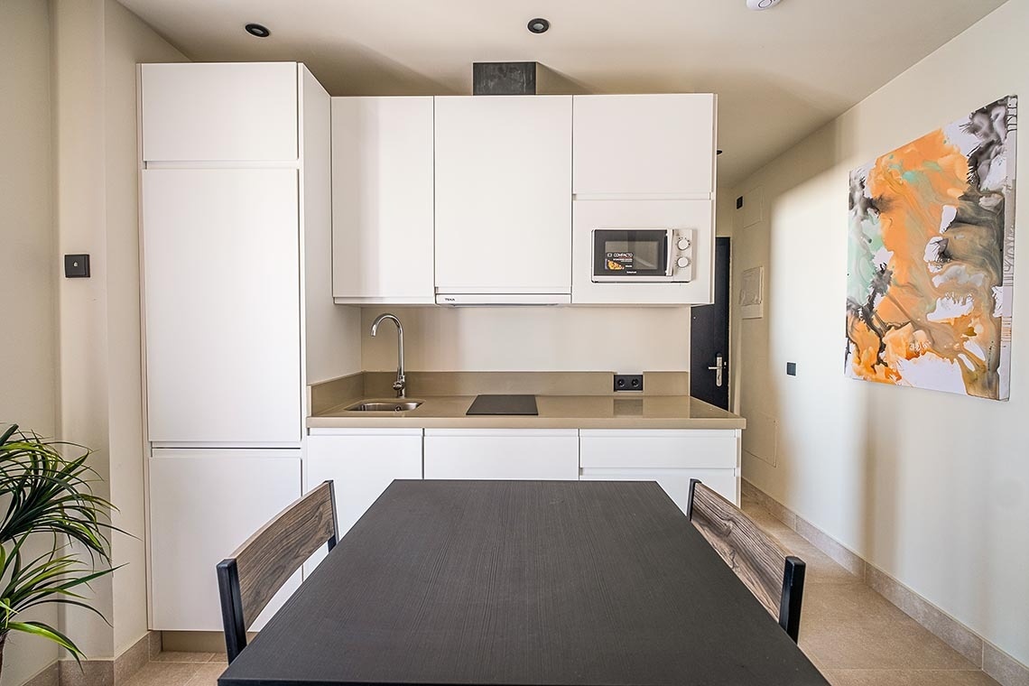 una pequeña cocina con gabinetes blancos y una mesa negra