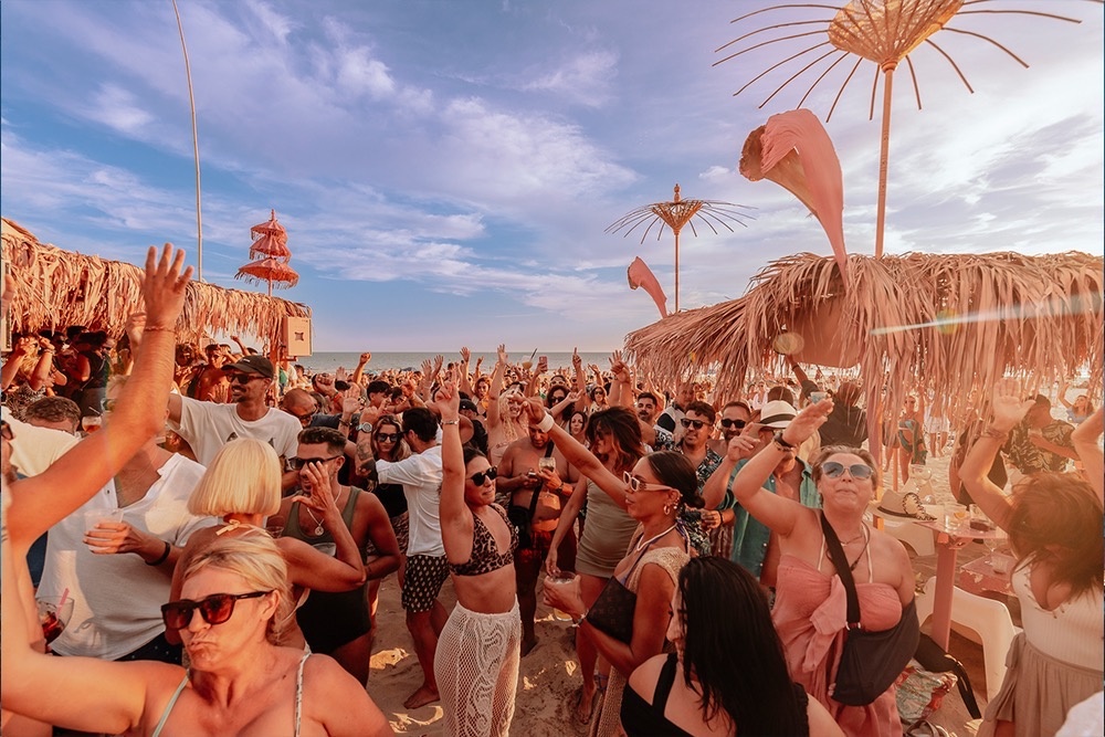 una gran multitud de personas bailan en una fiesta en la playa