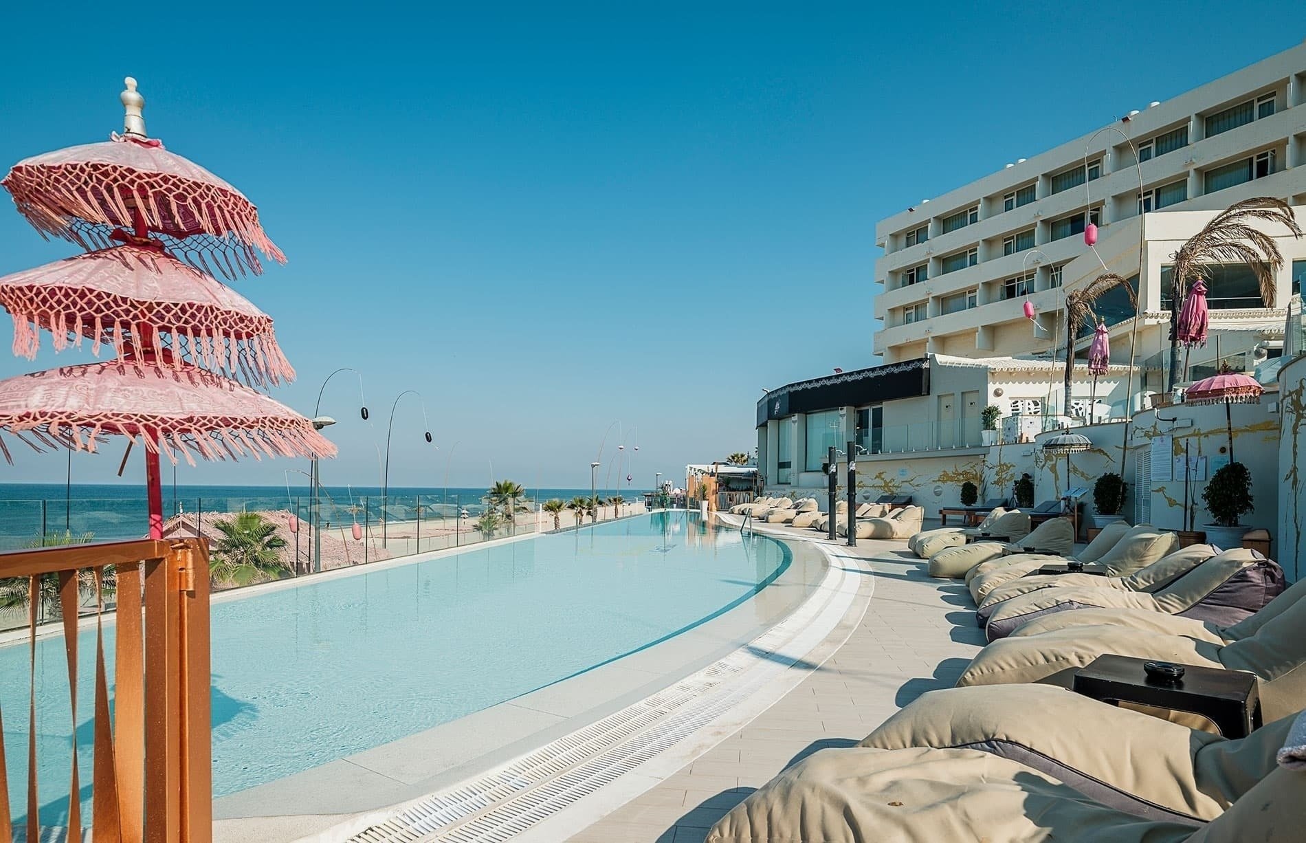 ein großer Pool mit Liegestühlen und Regenschirmen vor einem Hotel