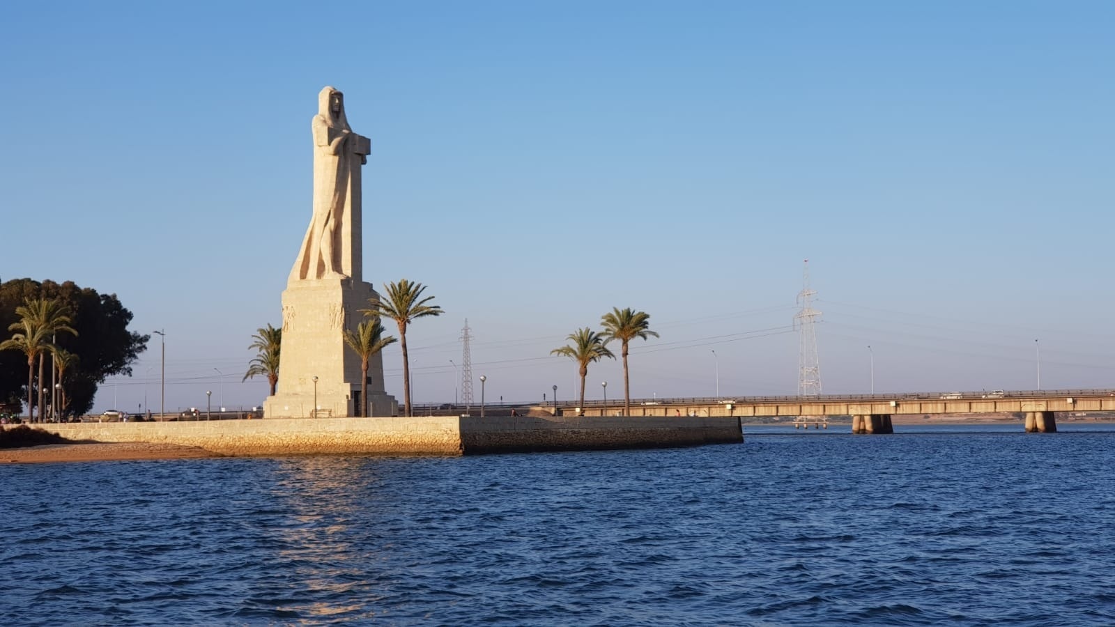 una estatua en la orilla de un río con un puente en el fondo