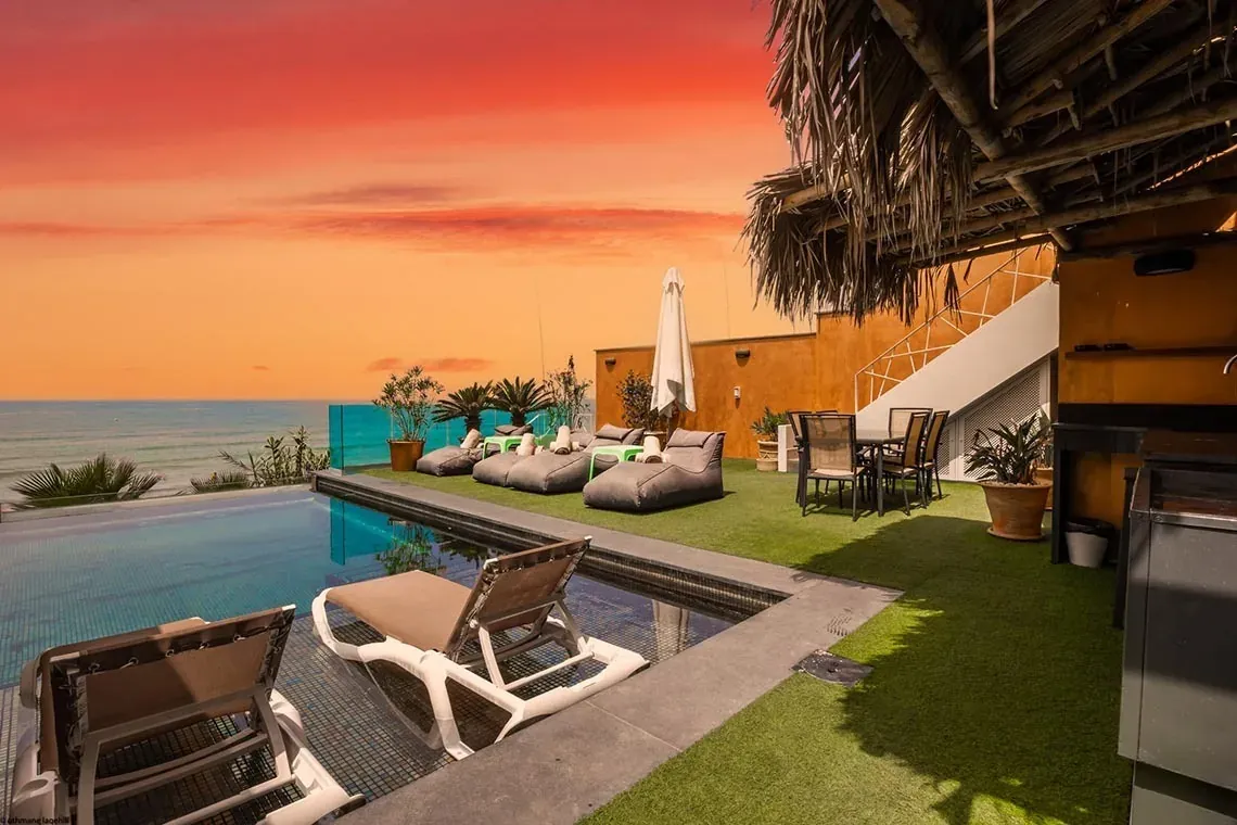 Terraza ON Village Matalascañas con piscina, tumbonas, y vistas al mar al atardecer.