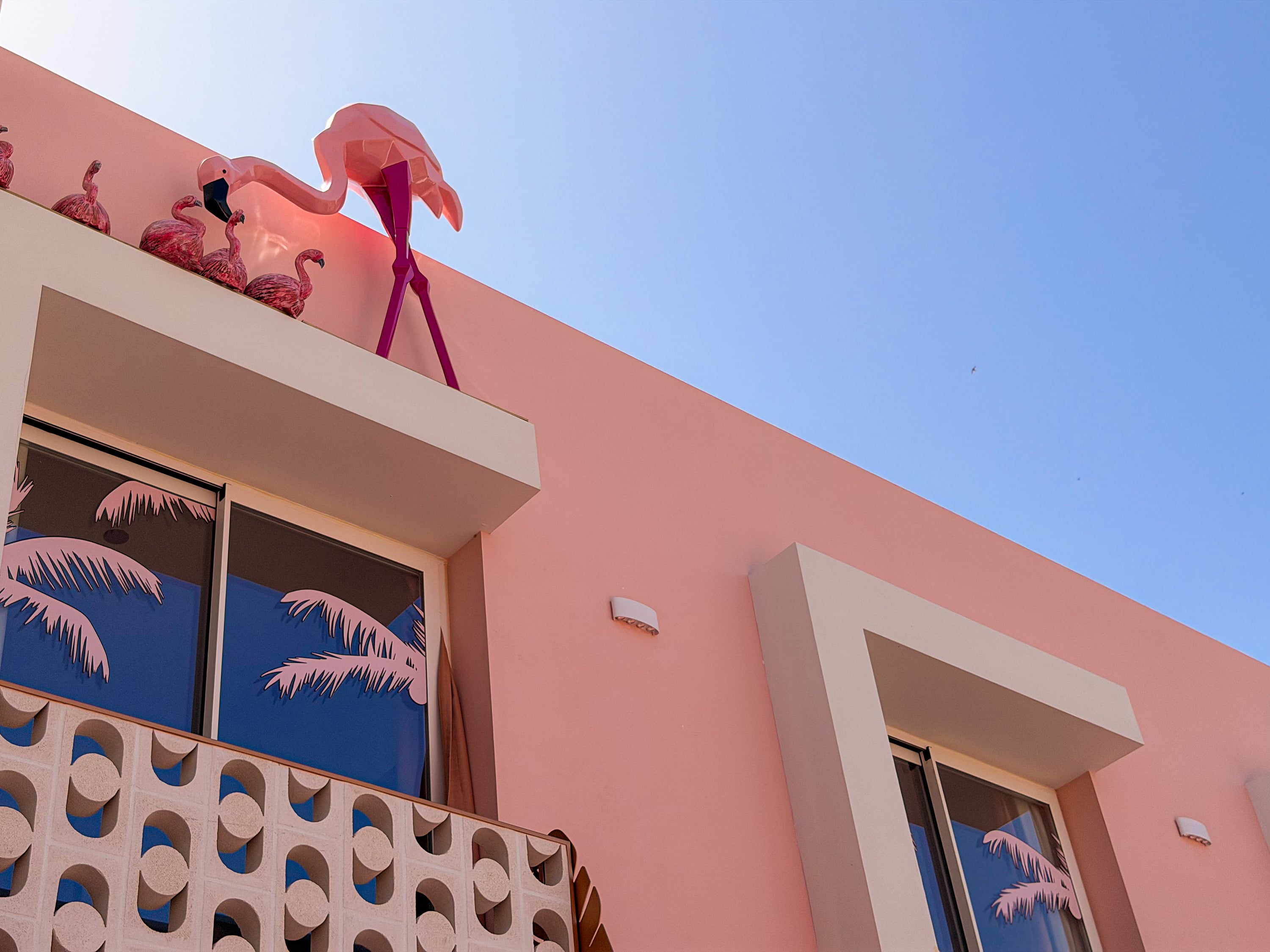 Fachada rosa de hotel con flamencos decorativos y palmeras en las ventanas, ideal para tu estancia ON Pink Motel | Matalascañas.