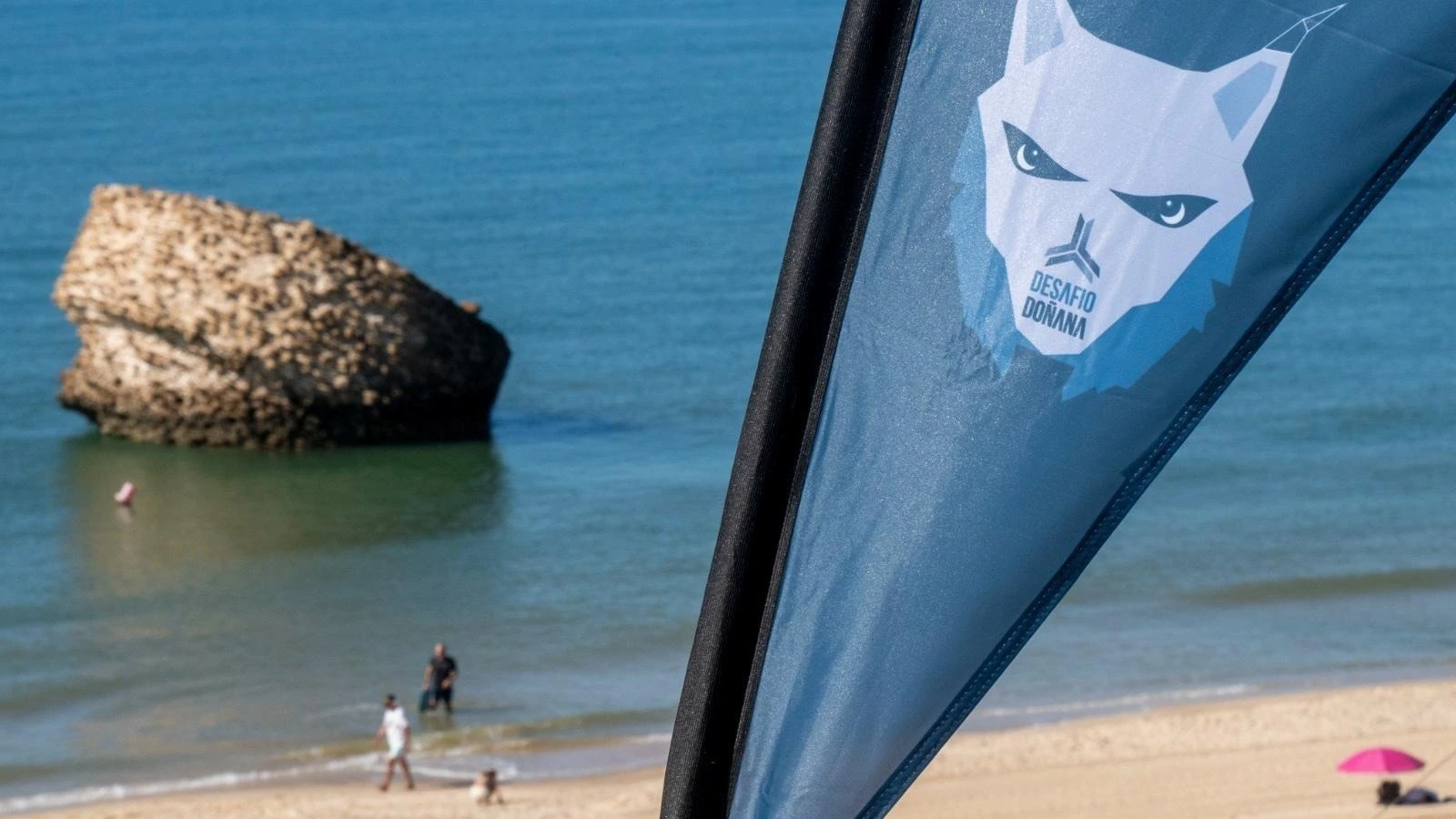 Strandflags mit @On Hotels Corporativa-Logo am Meer mit Felsen und Strandbesuchern