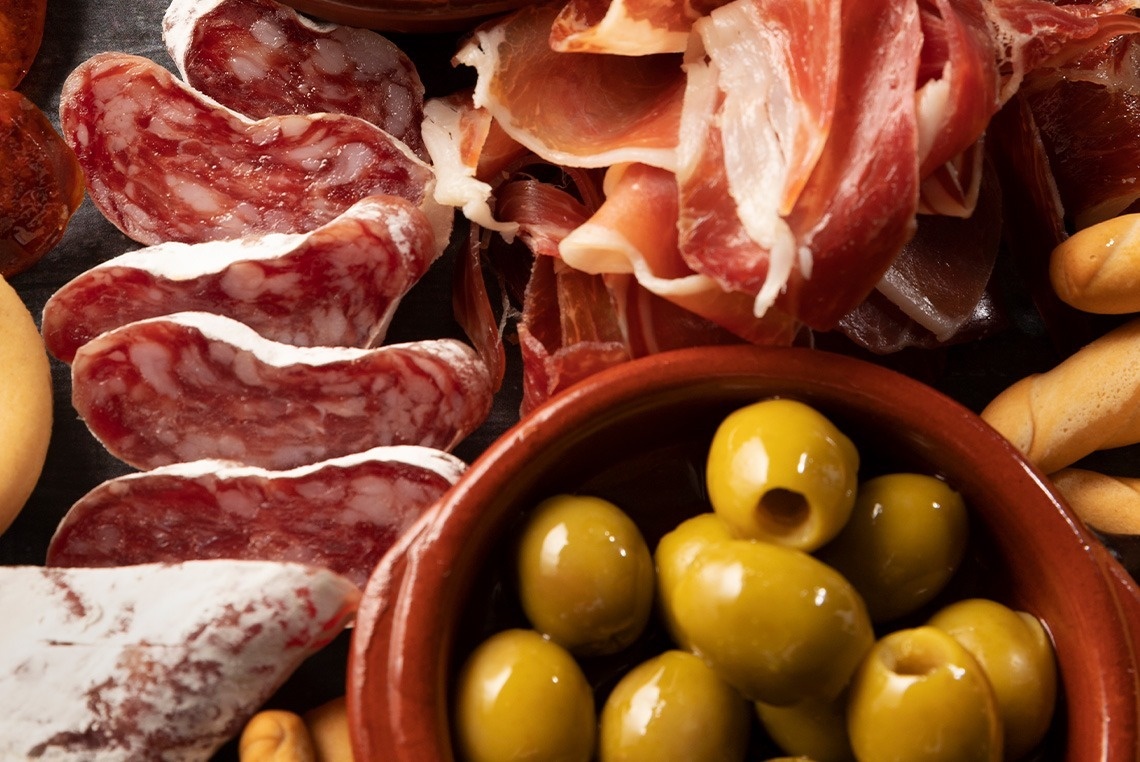 a bowl of green olives sits next to a plate of meat