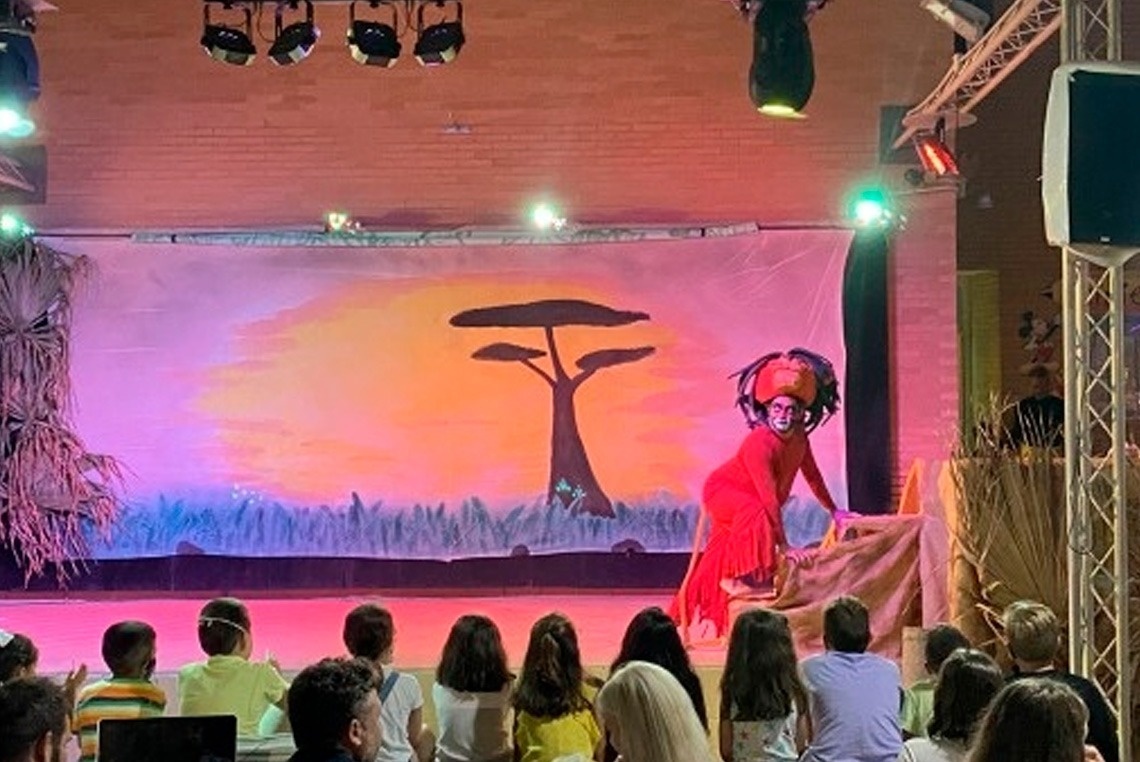 a group of people sitting in front of a stage with a tree on it