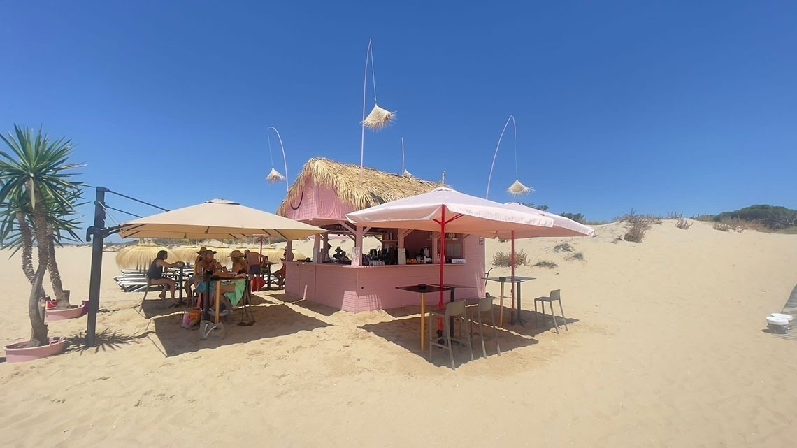 a pink hut with a thatched roof sits on a sandy beach