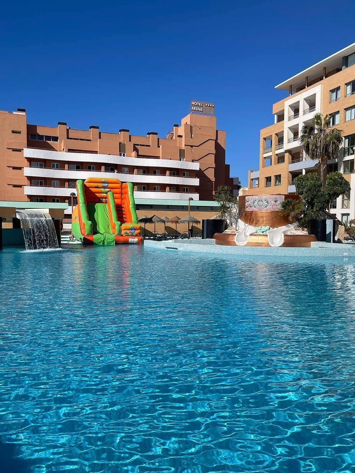 una piscina con un tobogán inflable y un hotel en el fondo