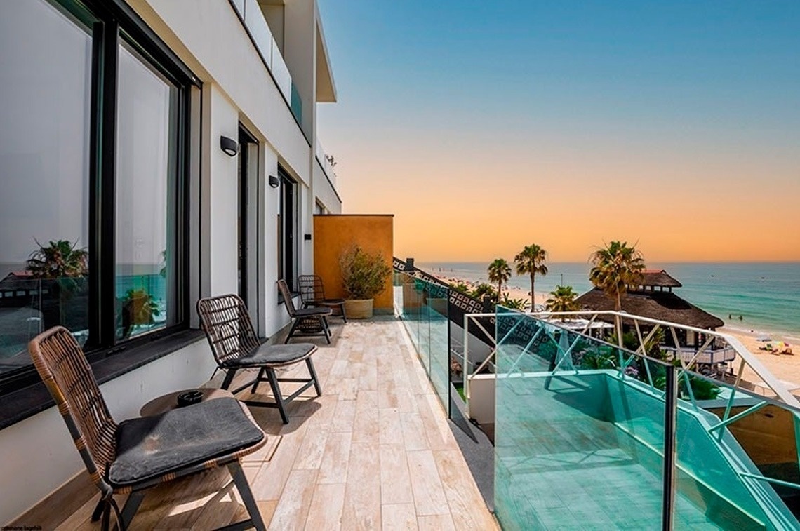a balcony with chairs and a glass railing overlooking the ocean
