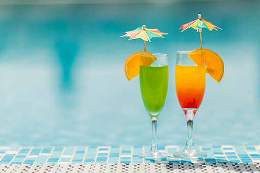 two drinks with umbrellas on top of them are next to a pool