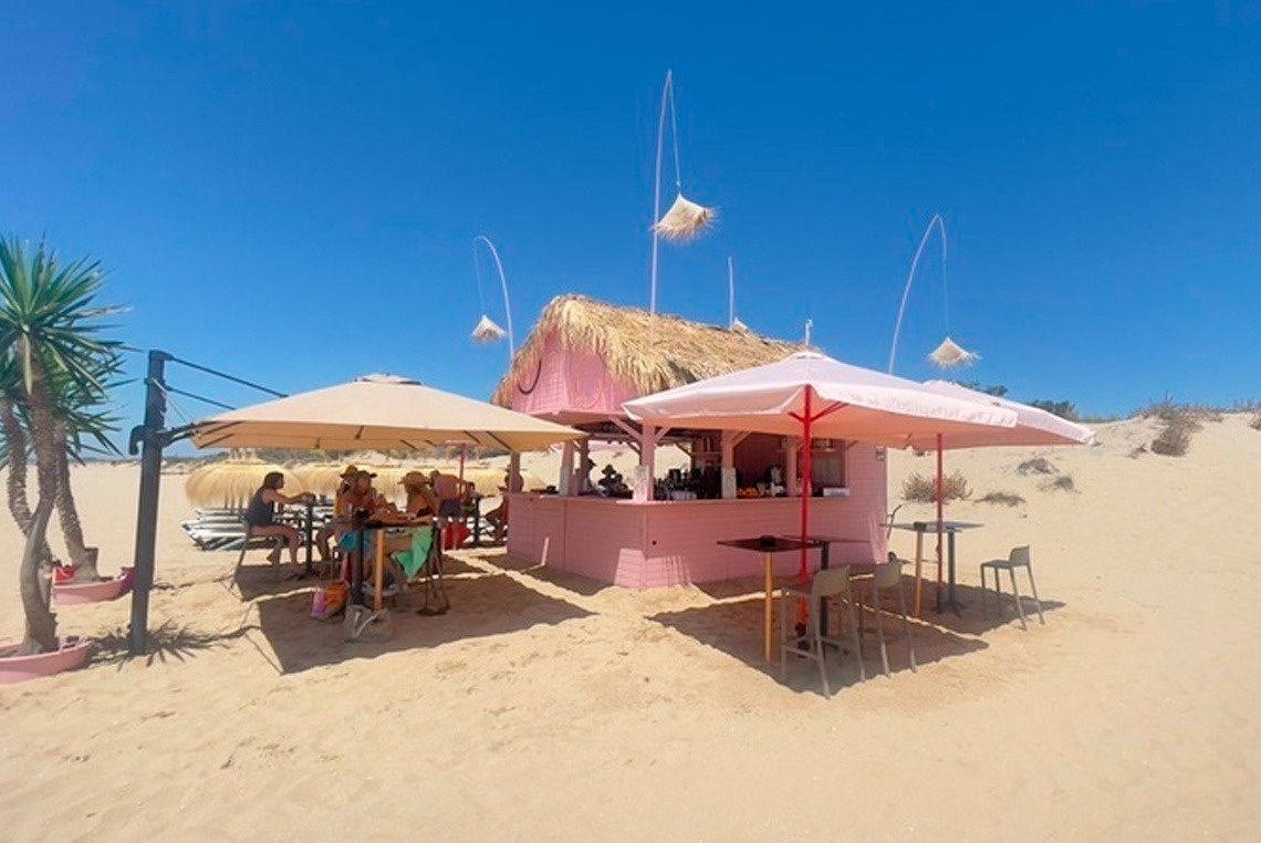un bar rosa en la playa con sombrillas y mesas