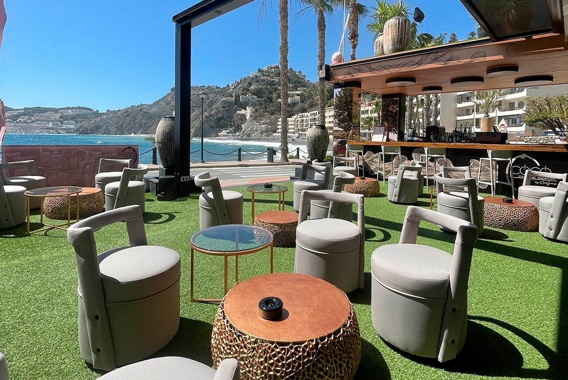 a patio area with tables and chairs with a view of the ocean