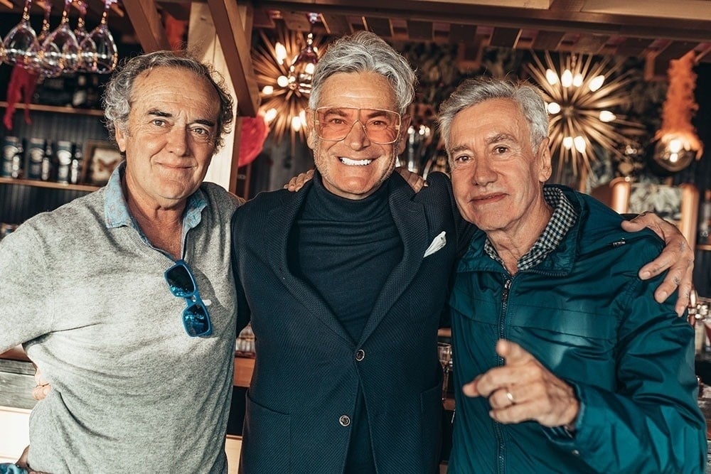tres hombres posan para una foto y uno de ellos lleva una chaqueta azul