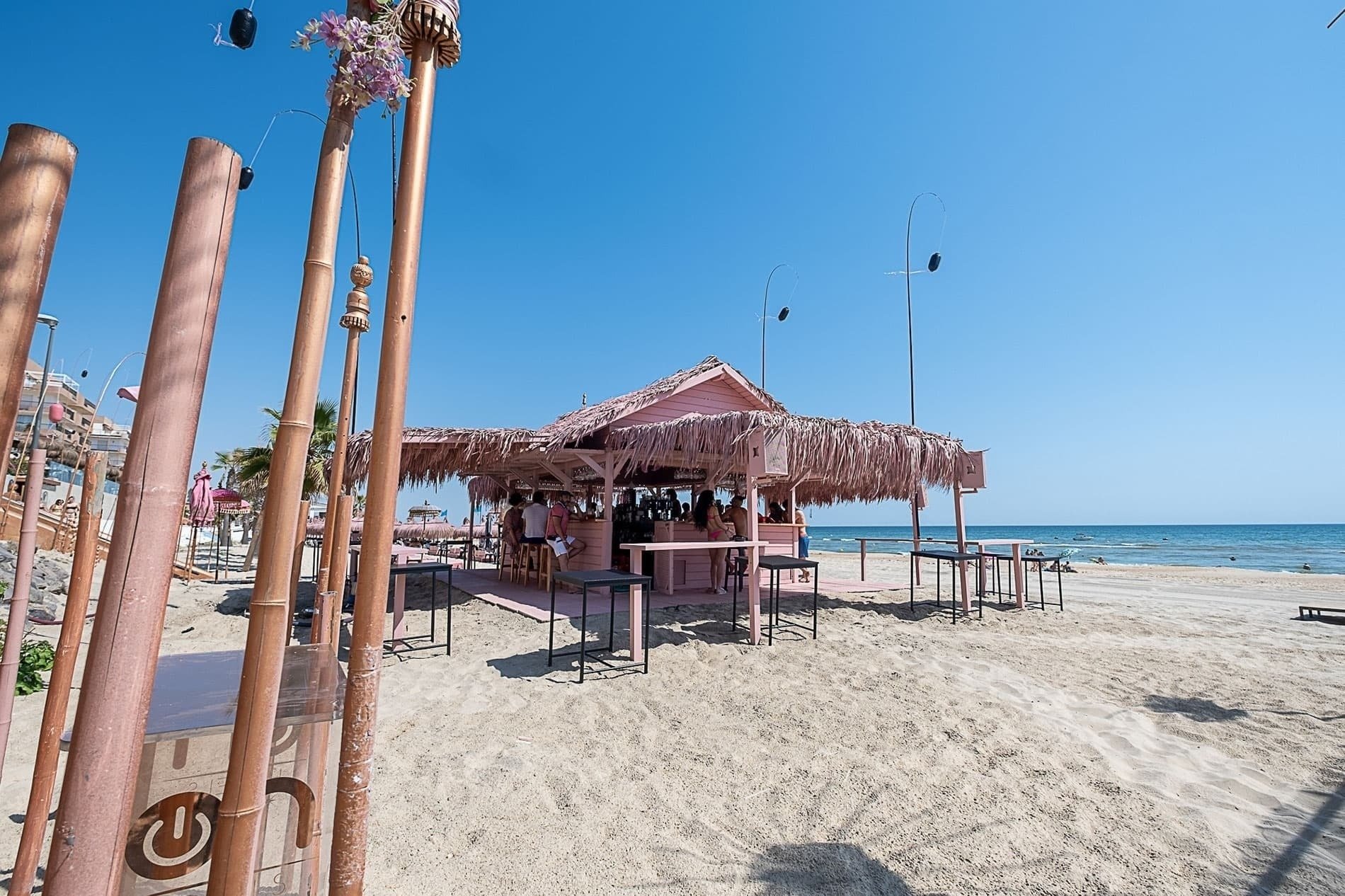 un bar rosa en la playa está rodeado de mesas y sillas