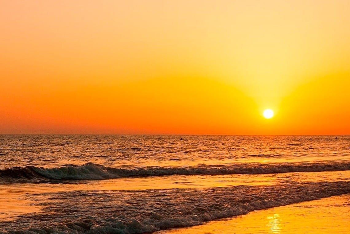 the sun is setting over the ocean and the waves are breaking on the beach