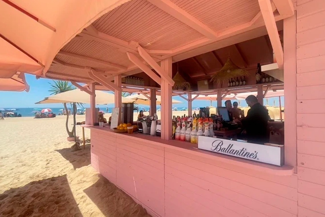 un bar rosa en la playa con un letrero de ballantine 's