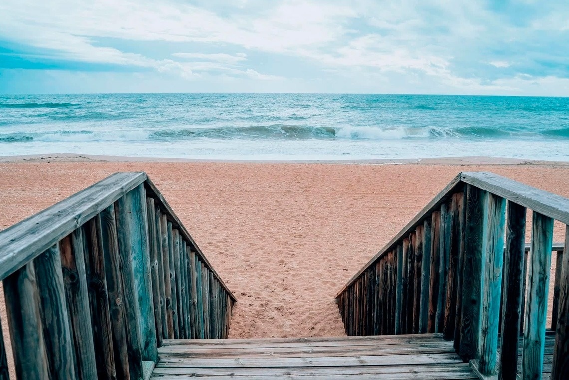 una escalera de madera conduce a una playa de arena al océano