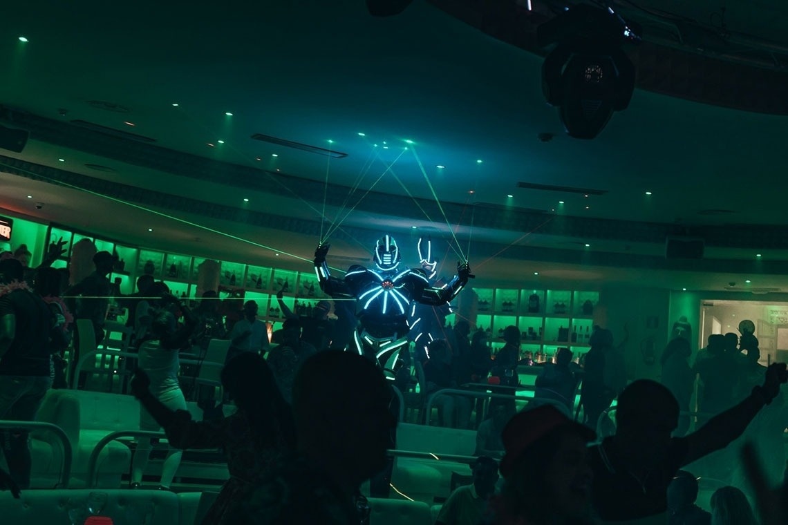 un grupo de personas bailan en una discoteca mientras un hombre con traje de neón brilla en la oscuridad