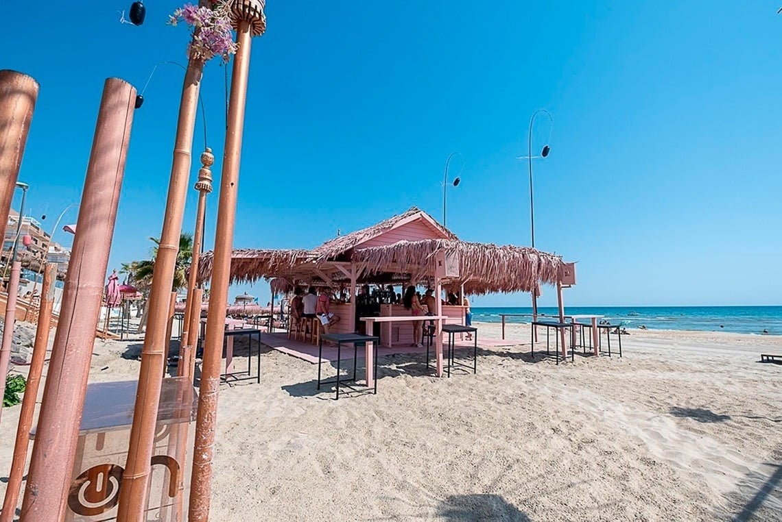 uma praia com um bar rosa e um sinal de g